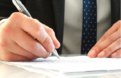Image of a hand holding a pen signing a paper